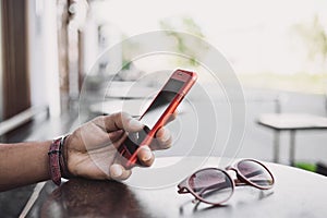 Young man texting on his smartphone in the city. Close up of adult hand using mobile phone at a cafe