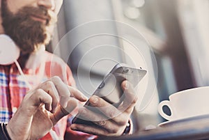 Young man texting on his smartphone in the city. Close up of cheerful adult using mobile phone in a cafe