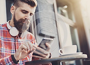 Young man texting on his smartphone in the city. Close up of cheerful adult using mobile phone in a cafe