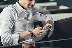 Young man texting on his smartphone in the city. Close up of cheerful adult using mobile phone in a cafe