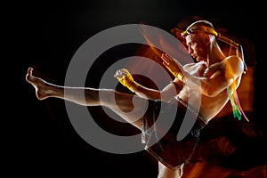 Young man thai boxer training over dark background in neon mixed light.