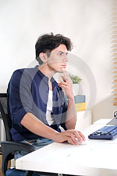 Young man thinking while working with computer at home office, work from home
