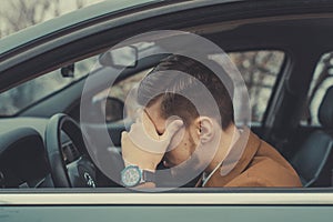 A young man of thirty years, holding his head, having a headache, driving a car. Poor health while driving