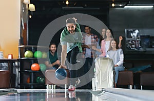 Young man throwing ball and spending time with friends in bowling