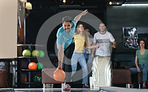 Young man throwing ball and spending time with friends in bowling