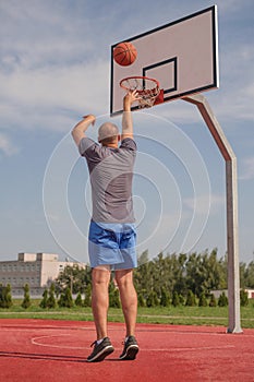 A young man throws a ball into basketball basket while playing on an playground