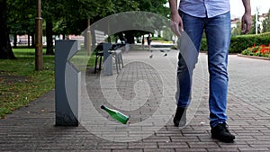 A young man throws a plastic bottle in the city near a trash can