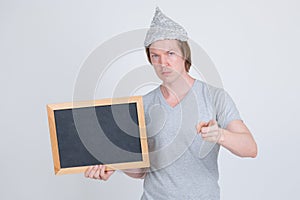 Young man with tin foil hat holding blackboard and pointing at camera