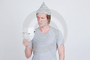 Young man with tinfoil hat as conspiracy theory concept holding white mask