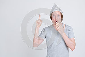 Young man with tinfoil hat as conspiracy theory concept pointing up and looking shocked