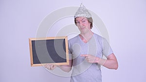 Young man with tinfoil hat holding and pointing at blackboard