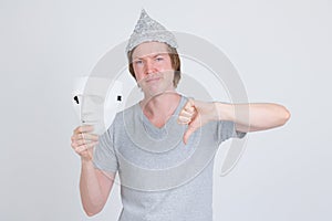 Young man with tinfoil hat holding white mask and giving thumbs down