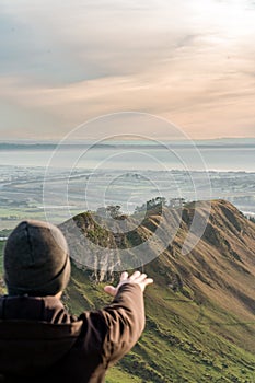 Young man at the top of a mountain extending his hand. Vertical photography