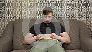 A young man touches his fat belly and then cries. The man on the couch slaps on his stomach. Gained excess weight in