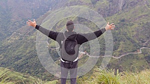 Young man tourist with backpack standing on the edge of beautiful canyon and victoriously raised hands. Male hiker