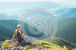 Young man tourist backpacker sits on top on hill with beautiful