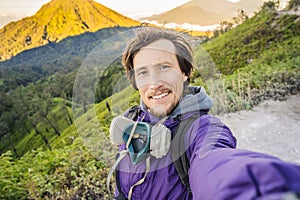 Young man tourist makes a selfie with the magnificent views on green mountains from a mountain road trecking to the Ijen