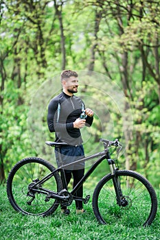 Young man in track-suit with bicycle drinking water at summer park
