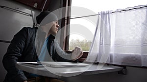 Young man in a train with laotop, looks out the window