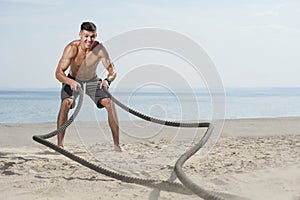 Young man training with battle ropes on the beach