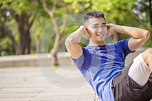 Young man training and doing sit ups  in park