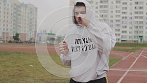 Young man training in hoodie boxing with invisible opponent at stadium.