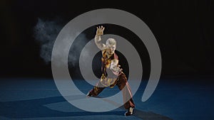 Young man training wushu against black background