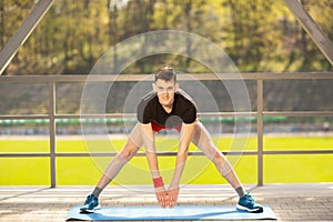 Young man training yoga outdoors. Sporty guy makes stretching exercise on a blue yoga mat, on the sports ground