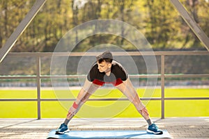 Young man training yoga outdoors. Sporty guy makes stretching exercise on a blue yoga mat, on the sports ground