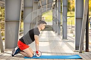 Young man training yoga outdoors. Sporty guy makes stretching exercise on a blue yoga mat, on the sports ground