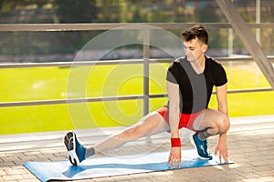 Young man training yoga outdoors. Sporty guy makes stretching exercise on a blue yoga mat, on the sports ground