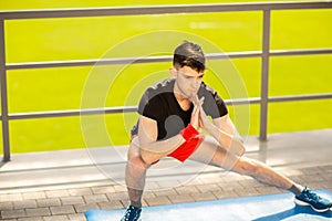 Young man training yoga outdoors. Sporty guy makes stretching exercise on a blue yoga mat, on the sports ground