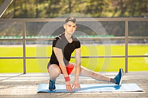 Young man training yoga outdoors. Sporty guy makes stretching exercise on a blue yoga mat, on the sports ground