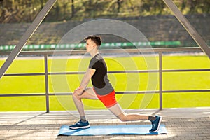 Young man training yoga outdoors. Sporty guy makes stretching exercise on a blue yoga mat, on the sports ground