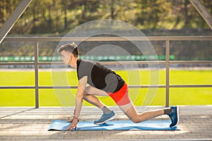 Young man training yoga outdoors. Sporty guy makes stretching exercise on a blue yoga mat, on the sports ground