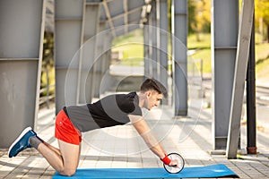 Young man training yoga outdoors. Sporty guy makes stretching exercise on a blue yoga mat, on the sports ground