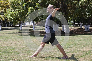 Young man training yoga outdoors. Sporty guy makes stretching exercise on a blue yoga mat, on the sports ground