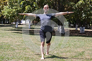 Young man training yoga outdoors. Sporty guy makes stretching exercise on a blue yoga mat, on the sports ground