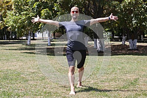 Young man training yoga outdoors. Sporty guy makes stretching exercise on a blue yoga mat, on the sports ground