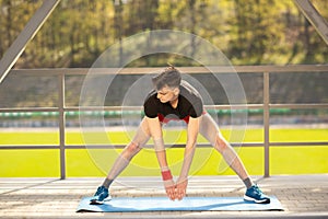 Young man training yoga outdoors. Sporty guy makes stretching exercise on a blue yoga mat, on the sports ground