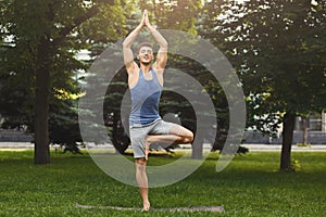 Young man training yoga in tree pose outdoors