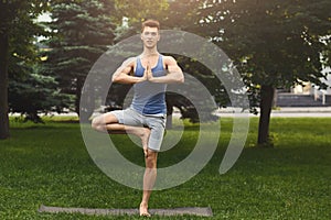 Young man training yoga in tree pose outdoors
