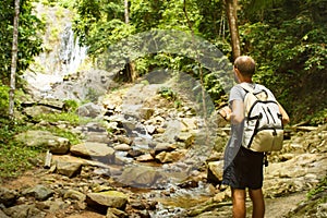 Young man with a travel backpack near a waterfall in Thailand