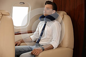 Young man with travel pillow resting while listening to music in airplane during flight