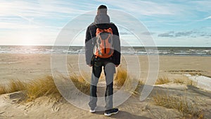 A young man traveler with a backpack stands on the beach and admires the view. Thinking about the future alone. Beautiful light