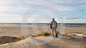 A young man traveler with a backpack stands on the beach and admires the view. Thinking about the future alone. Beautiful light,sa