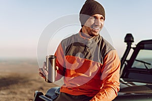 Young man traveler drinking from his thermocup while halt on a hike