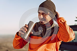 Young man traveler drinking from his thermocup while halt on a hike