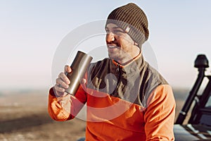 Young man traveler drinking from his thermocup while halt on a hike