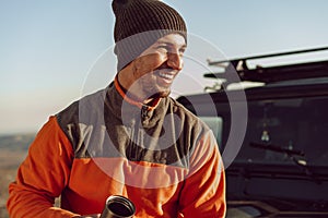 Young man traveler drinking from his thermocup while halt on a hike